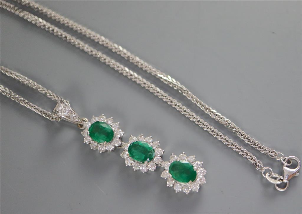 A modern 18ct white gold, emerald and diamond set oval triple cluster drop pendant, on an 18ct white gold chain,
